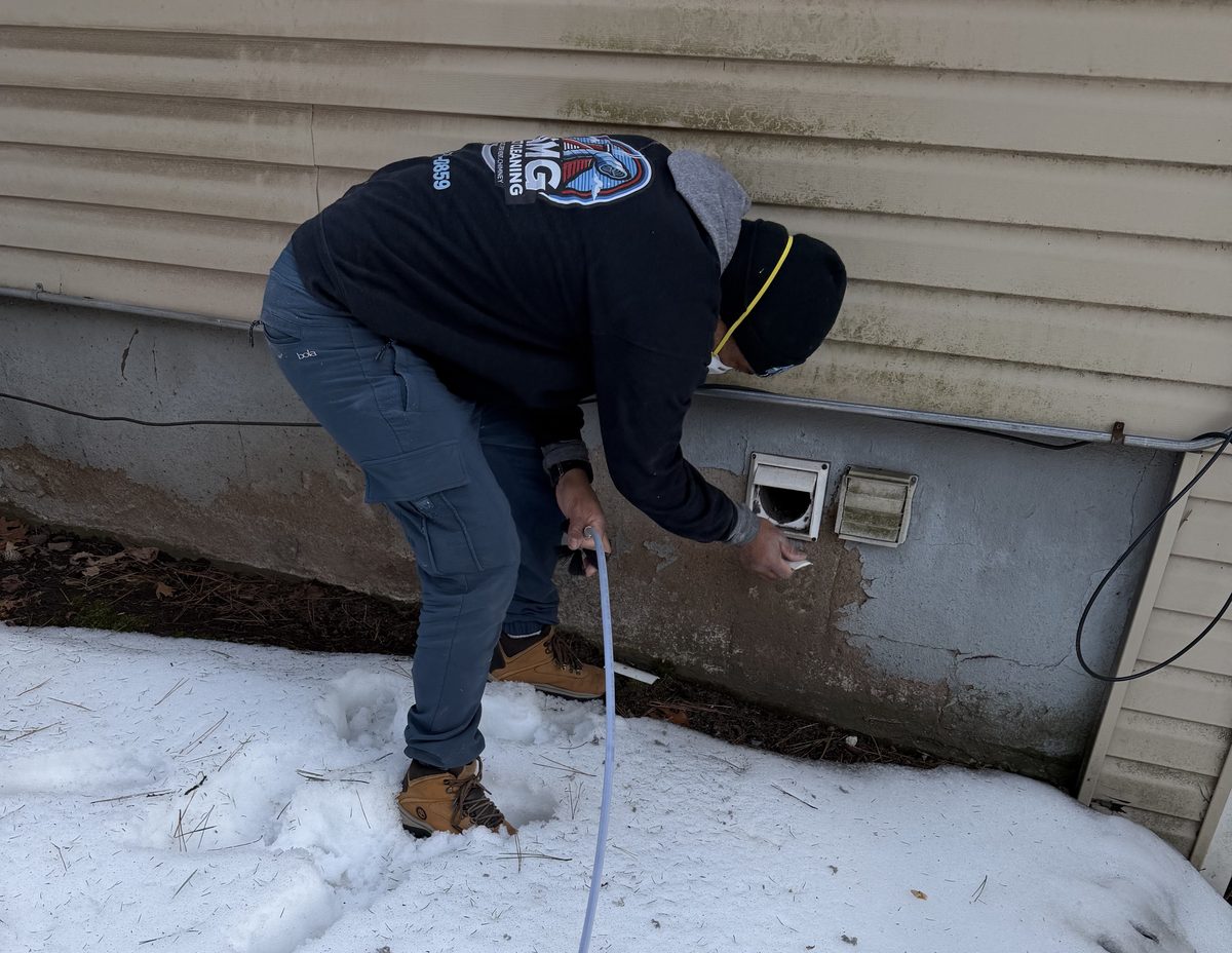 An AMG technician cleaning a dryer vent at a foundation wall in the snow