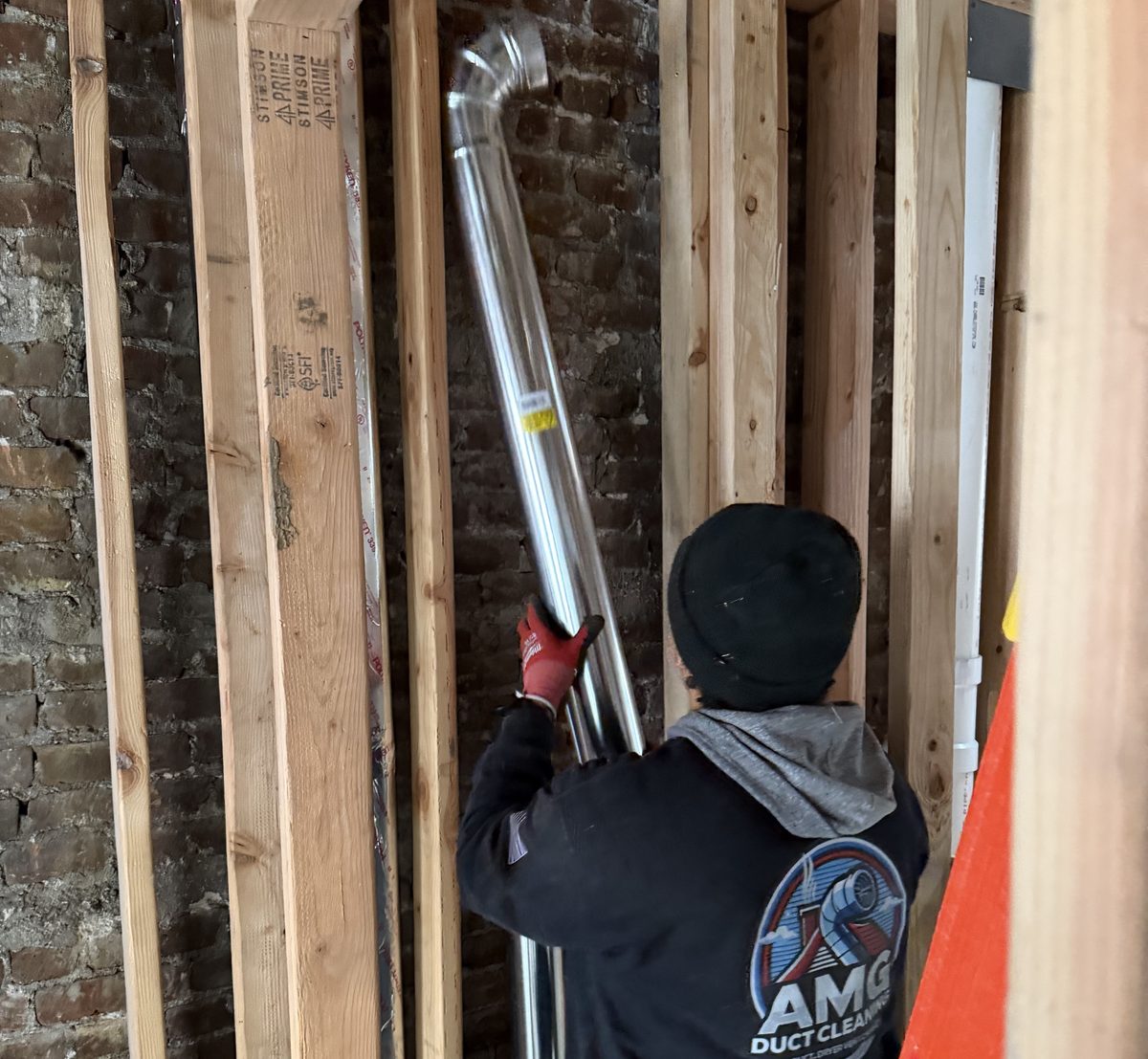 An AMG technician raising a run of round duct pipe inside open framing