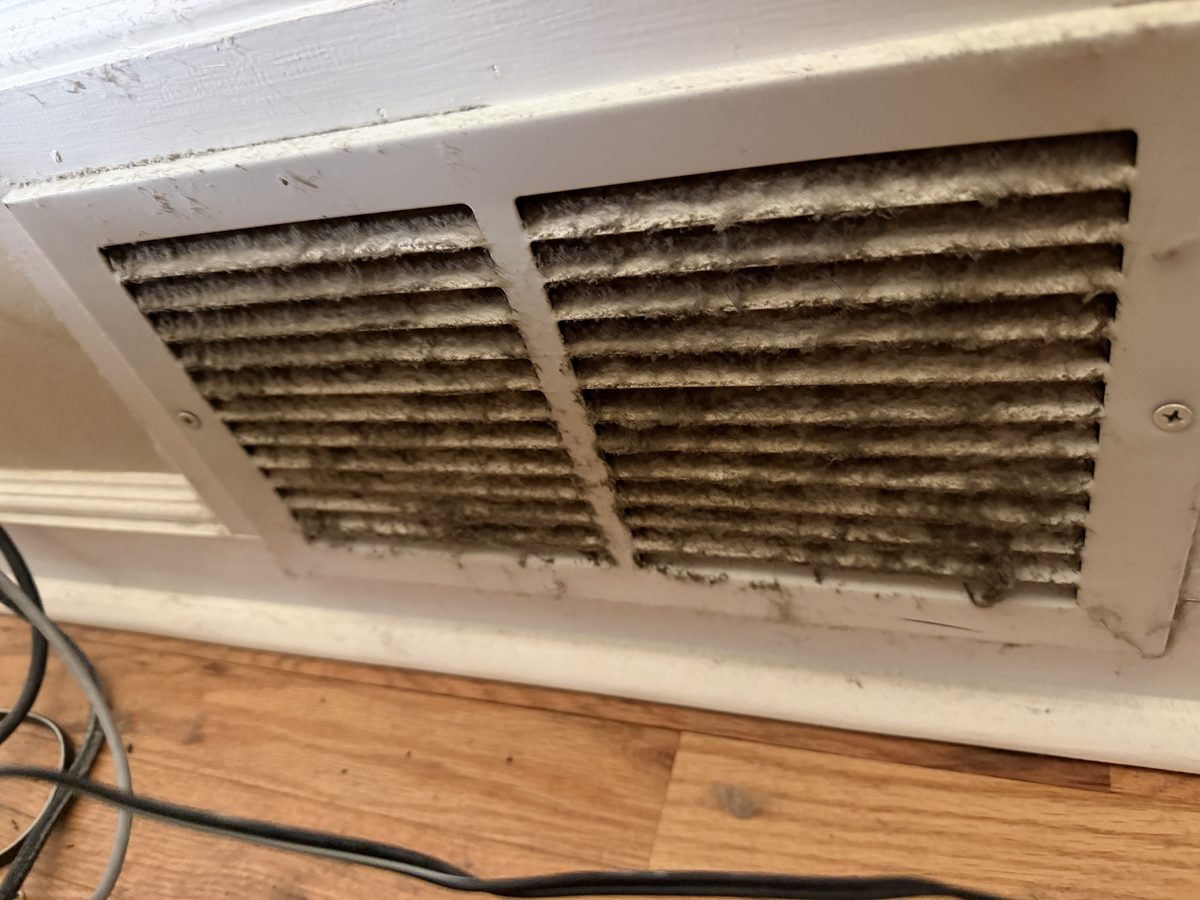 A wall return grille streaked with dust above the baseboard