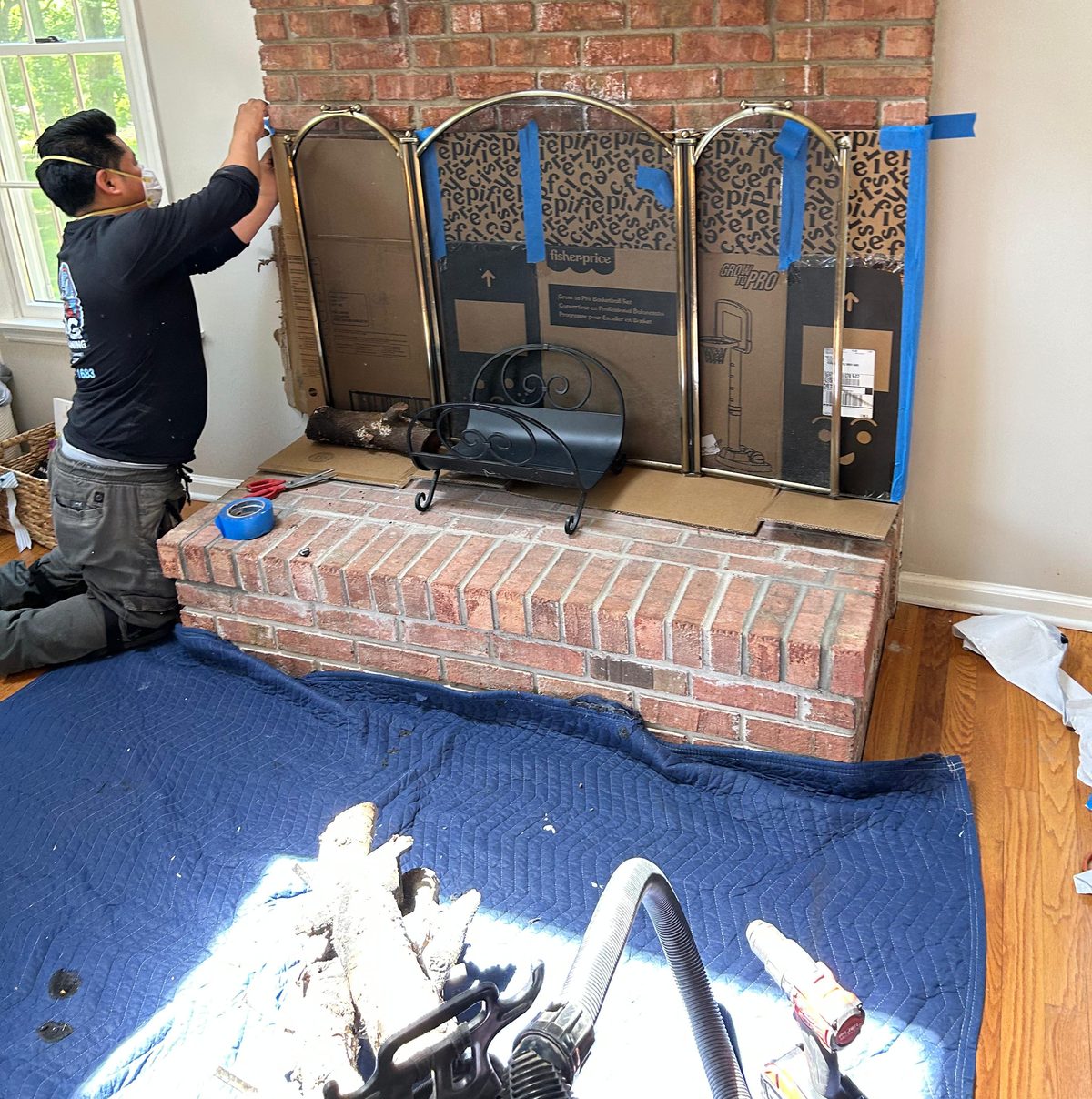 An AMG technician fitting a protective screen over a brick fireplace, a drop cloth across the floor