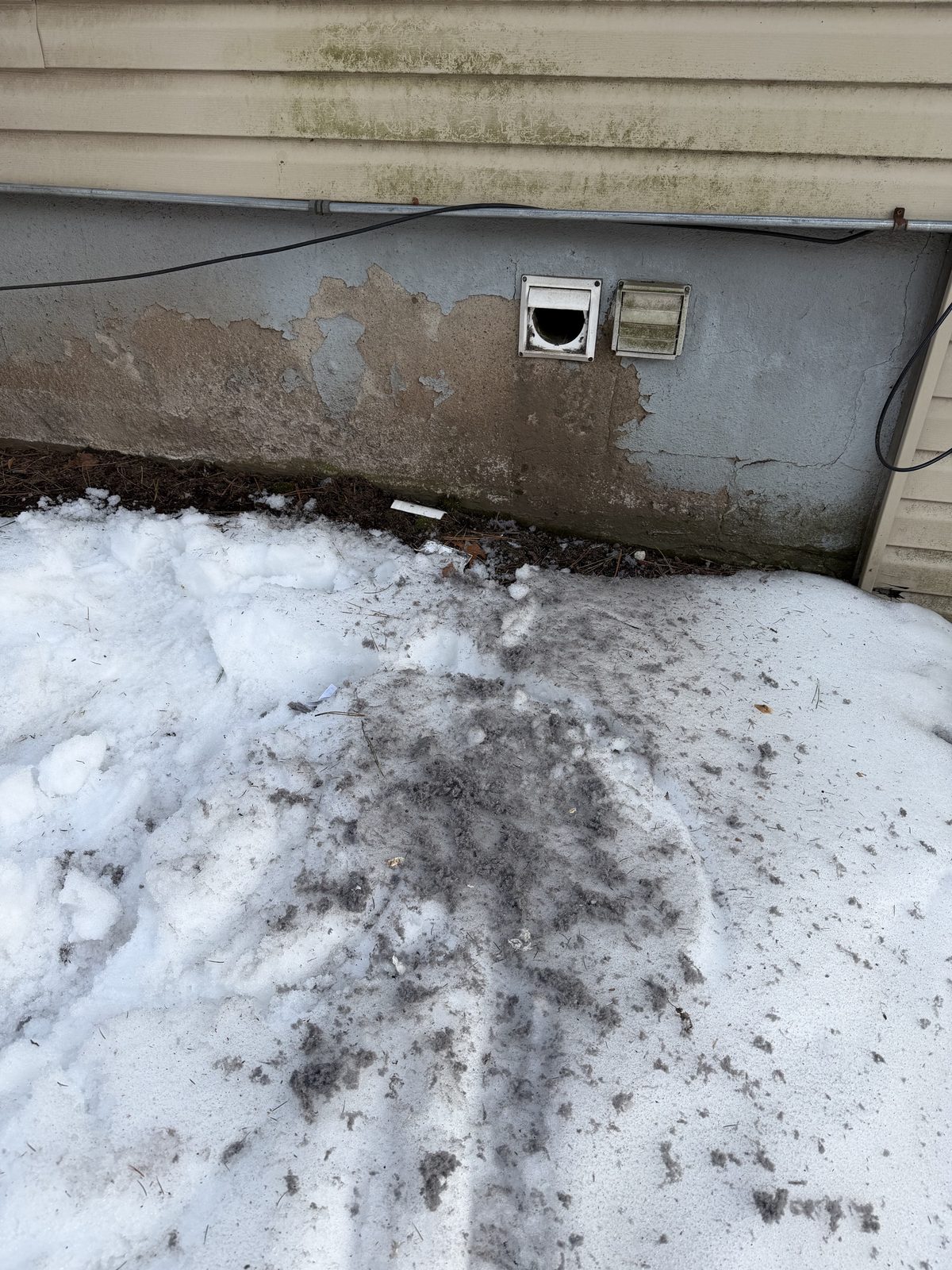Lint and debris blown out onto the snow below two vents