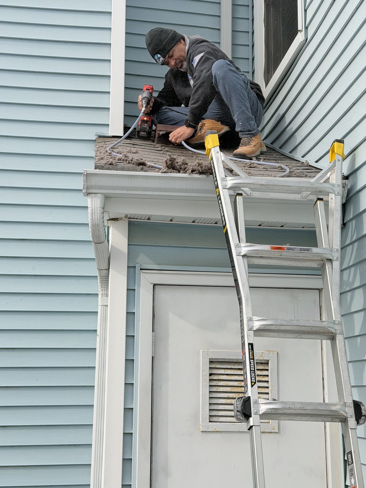 An AMG technician on a porch roof running a cleaning line, lint piled around him